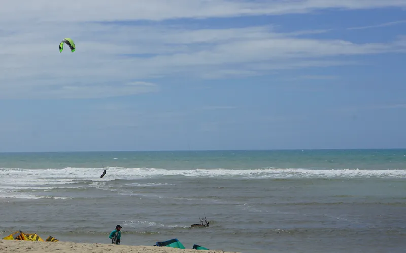 Praia de kitesurf no litoral do Ceará, com kite no ar e praticantes na água rasa — imagem ilustrativa